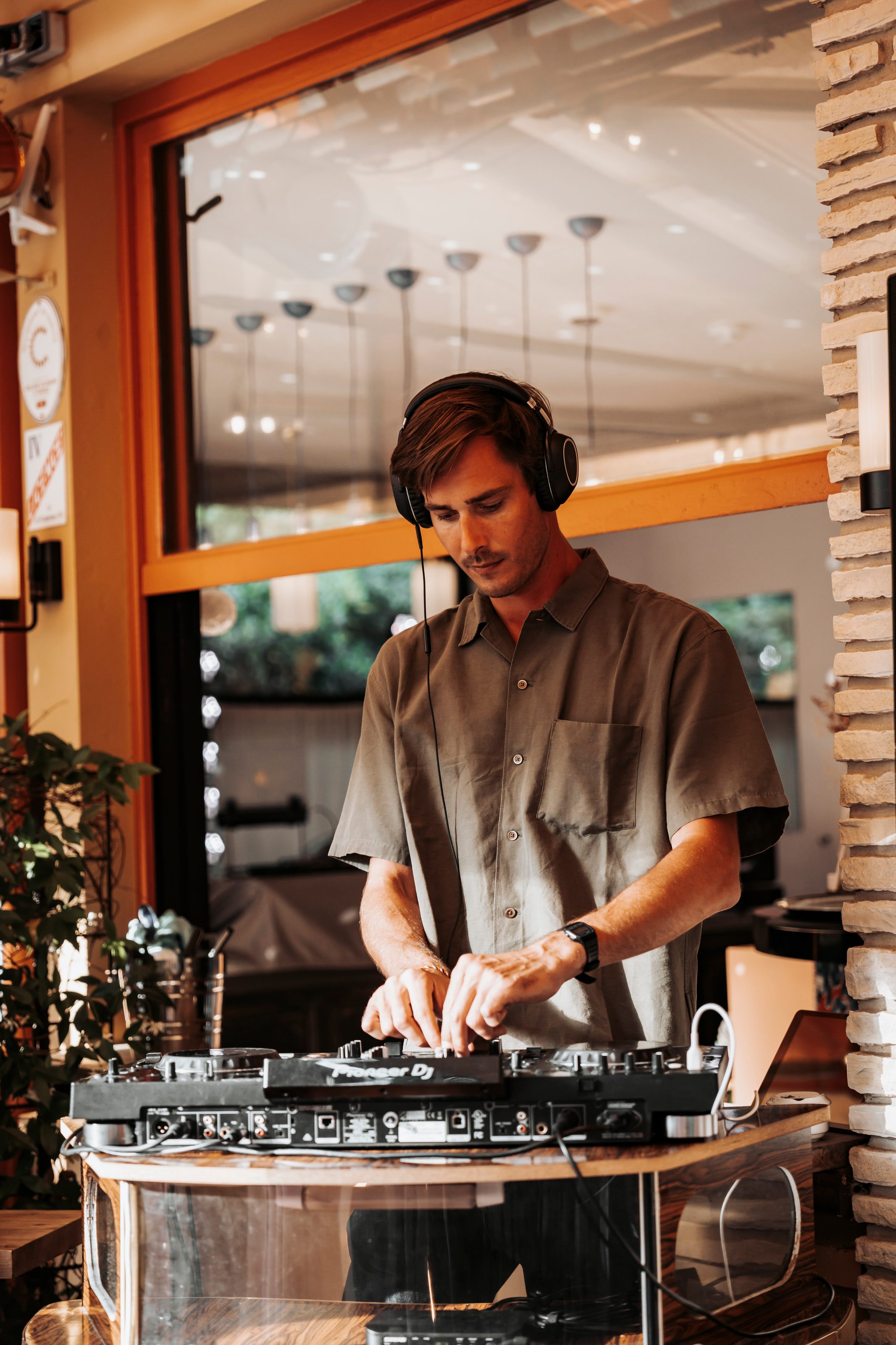 Black and white portrait of Victor Denver mixing at the decks, headphones on, beneath a canopy of pendant lights.
