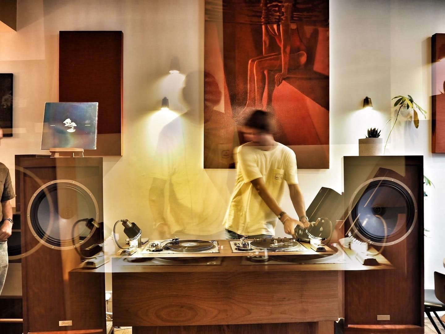Two turntables and a vinyl selection in a wood-panelled listening room with large loudspeakers.